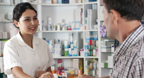 A female pharmacist smiling at a customer as she passes him some medication